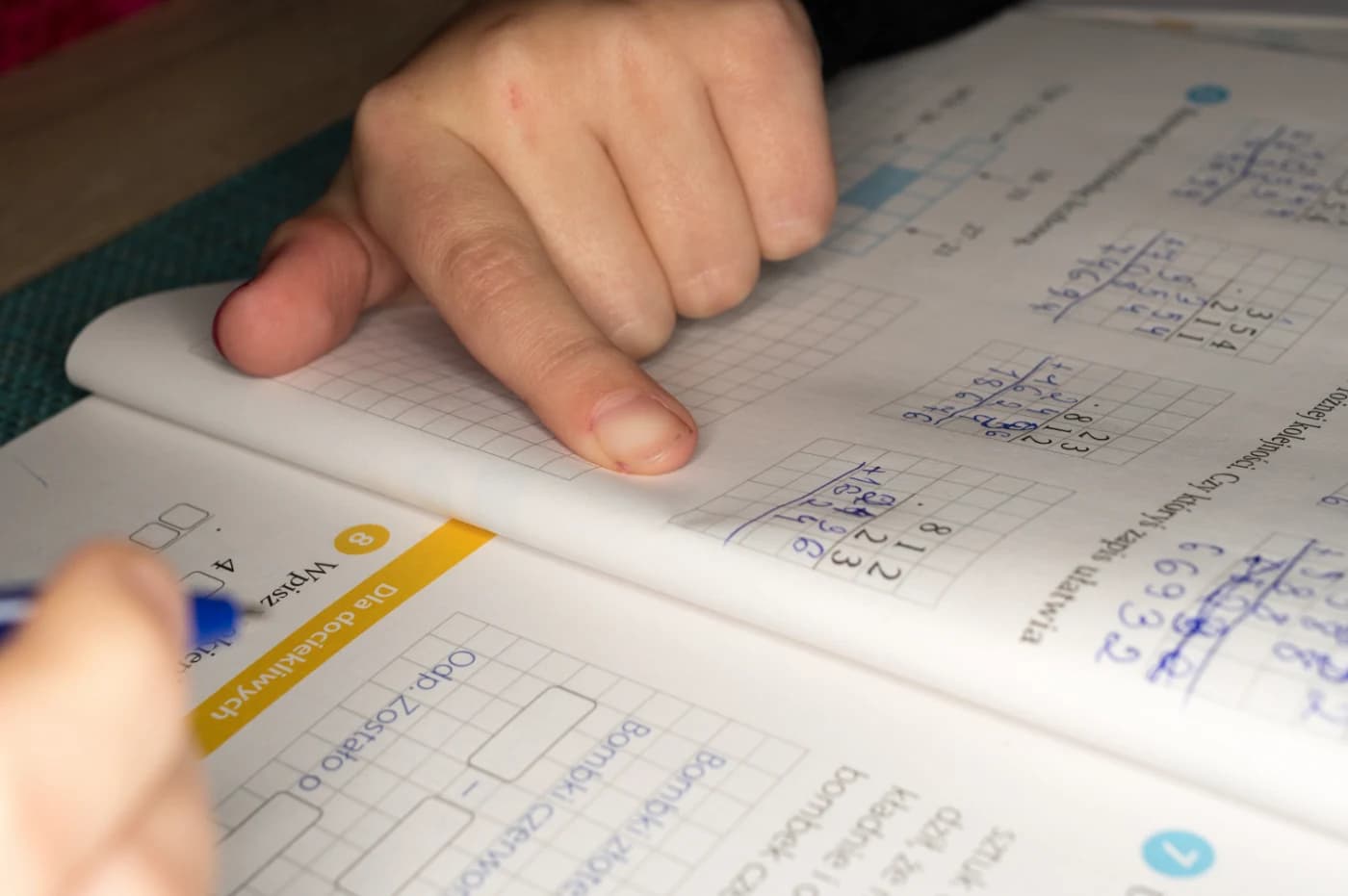Dziecko wskazujące palcem zadanie w otwartym zeszycie do matematyki.